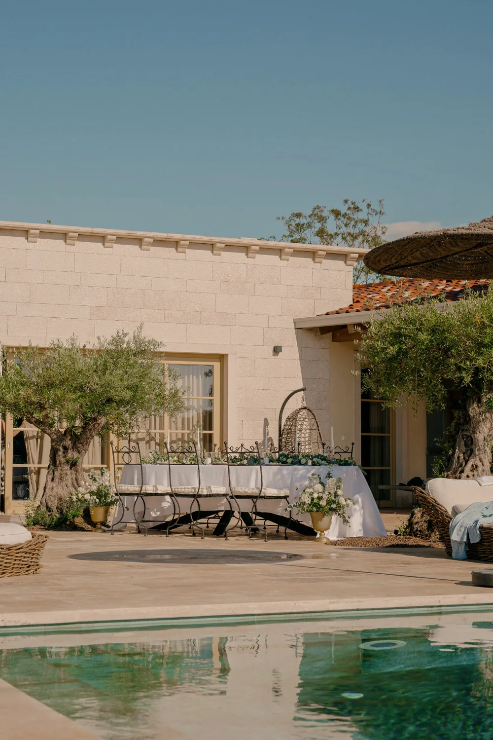 A dressed table beside the pool at LaMaison, olive trees and the house behind it