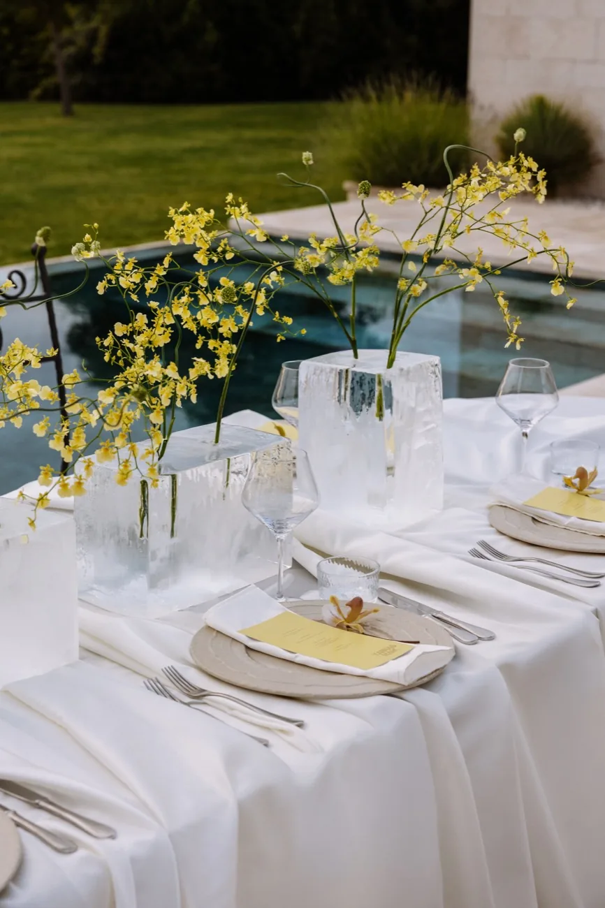 A table setting by the pool at LaMaison with yellow orchids in frosted vases